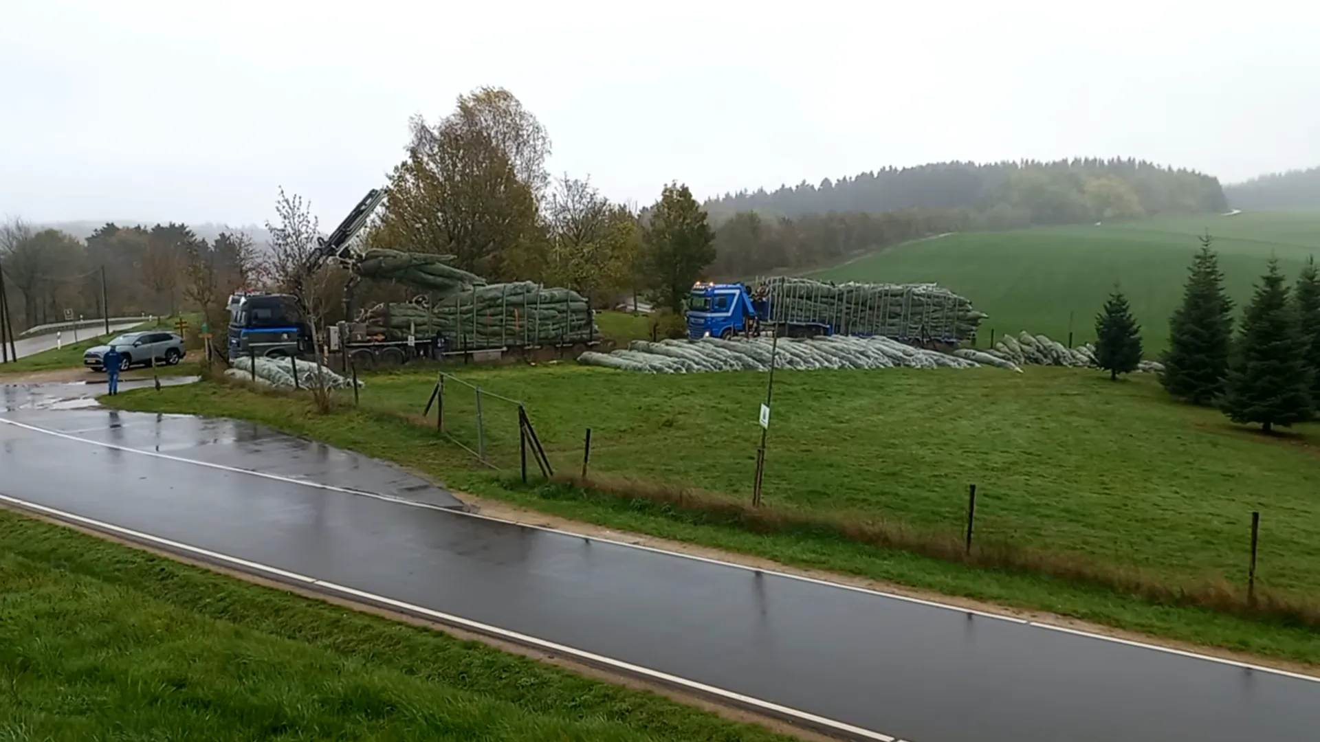 Rijdend beeld langs het opslagterrein met beladen wagens en kerstboompercelen.